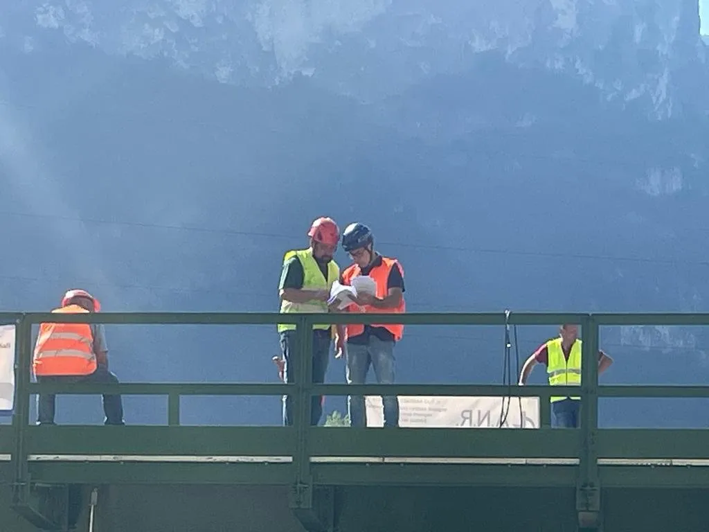 Tecnici con elmetto e gilet ad alta visibilità che consultano gli elaborati su un ponte in acciaio